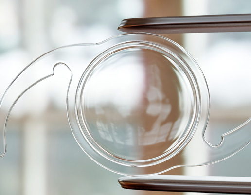 Nahaufnahme einer transparenten Teekanne mit rundem Körper und seitlichem Griff vor unscharfem Hintergrund.