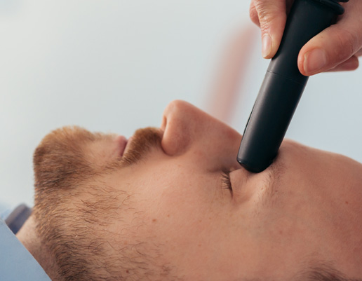 Hand hält schwarzen Rasierapparat über Gesicht mit Bartstoppeln.